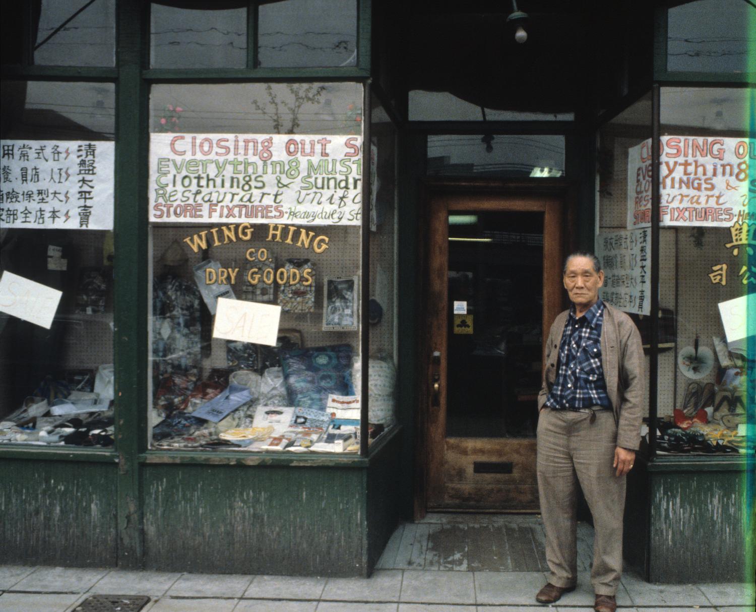 Wing Hing Dry Goods owner Lin Bei-lian standing at the front entrance to his shop prior to the business’s final closure. In the 1970s and 1980s, Yee photographed many Chinatown buildings and businesses to document changes in the neighbourhood’s landscape. Photographer: Paul Yee. Reference code AM1523-S6-F72-: 2008-010.0489.