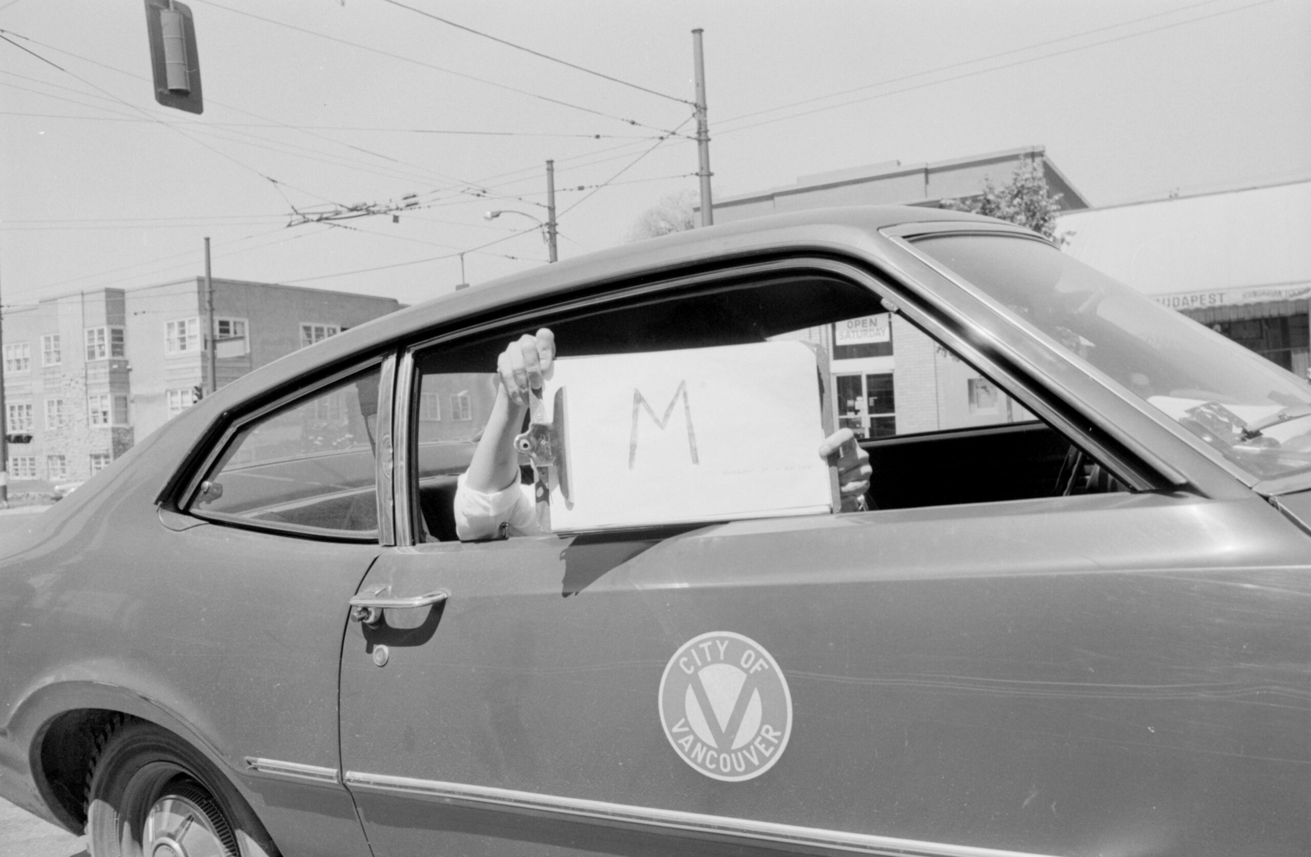 Person holding "M" sign out of a City of Vancouver car. Reference code: COV-S505-1-: 2019-103.0314